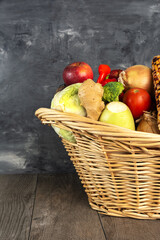 wicker basket with vegetables and fruits against a gray wall. Space for text.