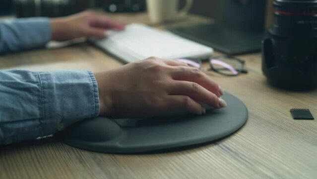 Close-up of hand of woman or female freelancer using computer mouse and clicking, while surfing the internet in spare time or working remotely from home.