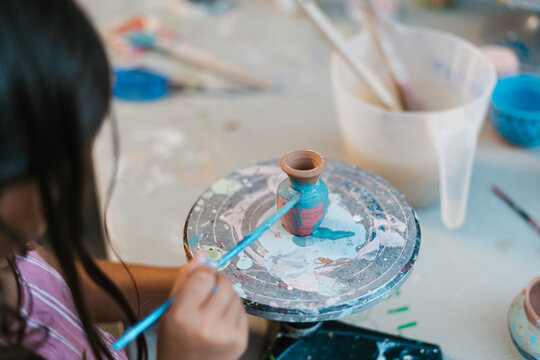 Faceless girl painting on clay vase