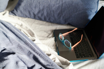 Unmade bed with laptop and reading glasses