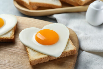 Heart shaped fried egg and toast on wooden board, closeup