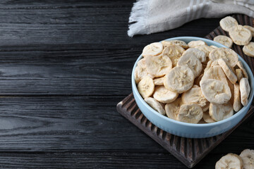 Bowl and dried banana slices on black wooden table. Space for text