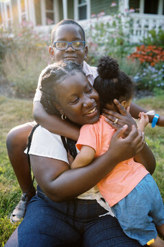 Happy Young Mother Playing With Two Children In The Front Yard Of Home