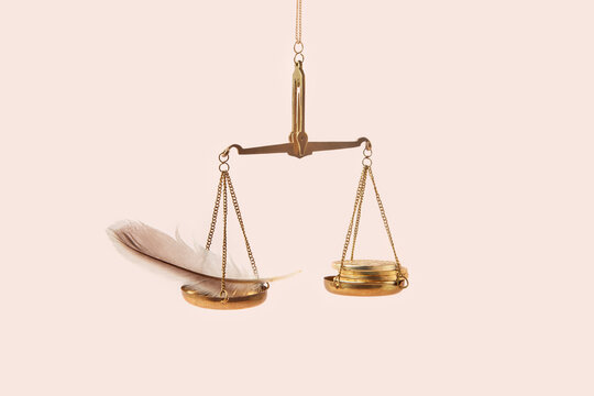 Golden coins and feather on weighing scale.