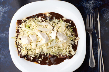 Chicken enmoladas covered with fresh cheese, lettuce and cream, made with corn tortilla