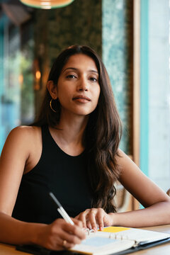 South Asian woman making notes and looking at camera
