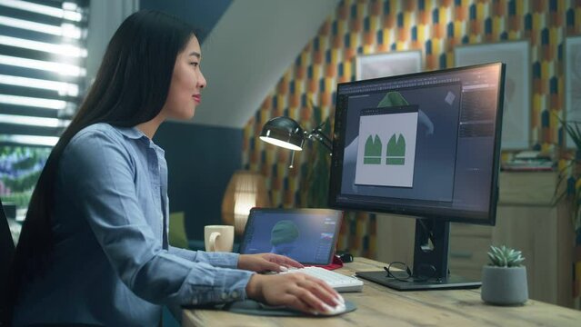 Asian woman creating 3D models of clothes on computer and tablet in 3D modeling program, while sitting at the desk and working remotely at home office.