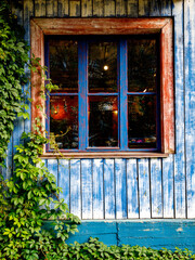 Fototapeta na wymiar Window with wooden window binding, lights and ivy leaves, blue neutral colour wall. Traditional European old town building. Old ancient historic architecture. Close up, vertical, Novosibirsk, Russia