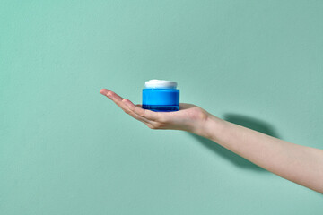 beautiful female hand holding a jar of cream on a blue