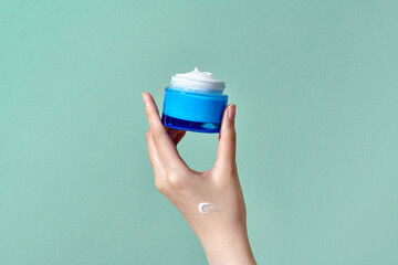 Woman's hand holds a round jar of body cream