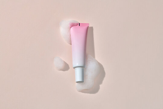 pink cosmetic tube on a beige background with soap foam and bubbles.