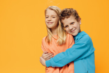 cute, joyful, loving school-age children stand on a yellow background and gently hug each other. theme of friendship and relationships