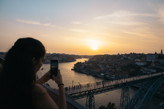 Young woman taking pictures with smartphone of the sunset in Porto