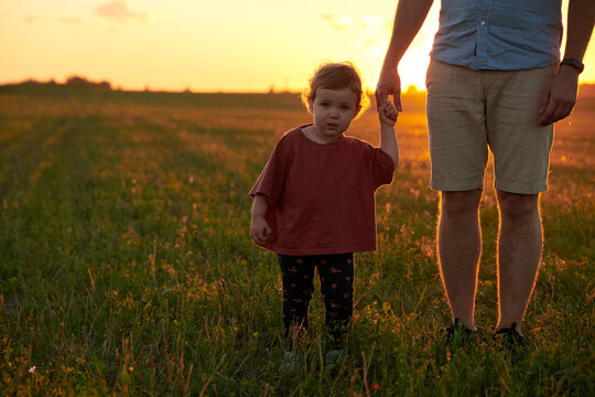 Baby girl walks hand in hand with dad at sunset