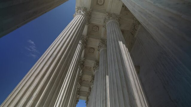 Wide angle pushing through very large towering columns in front of US Supreme Court building in Washington, DC showing judicial power over people and business.