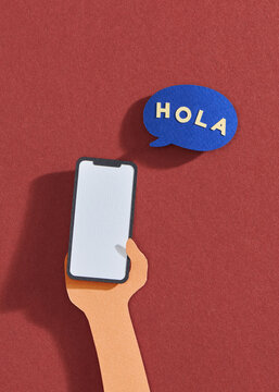 Mobile phone in hand and speech bubble, text hola