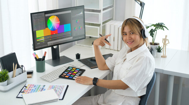 Smiling asian female graphic designer wearing headphone sitting front of computer sat her home office.