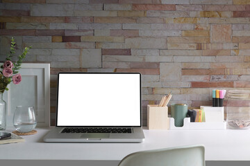 Home office desk with laptop, coffee cup, picture frame and stationery on white table..