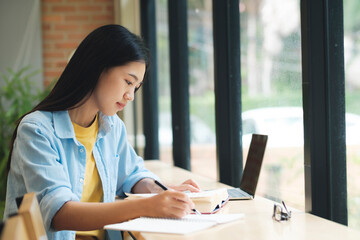 Young asian woman sitting at table and writing on notebook.