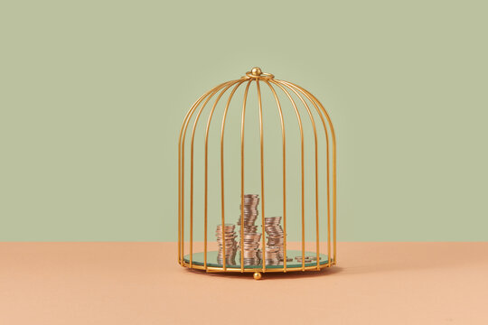 Golden birdcage with stacks of coins inside.