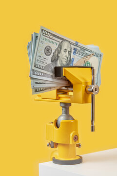 Dollar banknotes being squeezed by yellow clamp.