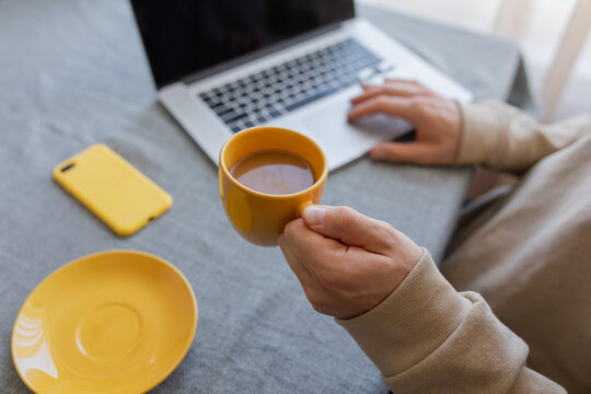 a mug with coffee in a man's hand in the background a laptop
