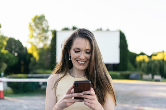 Smiling woman using smartphone at drive-in movie theater