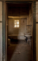 Antiguo baño abandonado con una tina ducha, lavamanos de loza y una pequeña ventana con reja. Luz tenue y sombras agradables