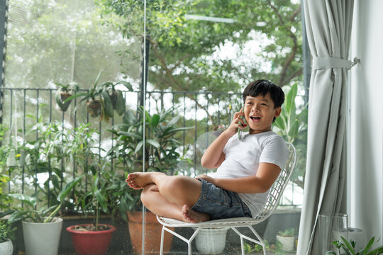 A Cute Smiling Preteen Boy Kid Sitting On A Chair Talking On Phone