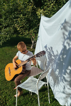 A boy is playing guitar in the garden.