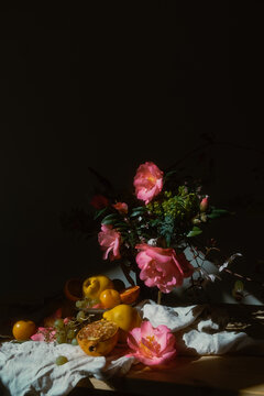 a bouquet of pink camellias on a table and many fruits on it