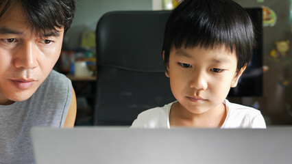 Authentic asian child boy using laptop with father. Kid looking to notebook for studying at home. Education learning, good family relationship, togetherness, home school concept.