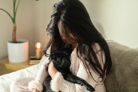 Brunette woman holding cute pug in bedroom