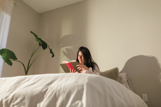 Young woman on duvet reading in bedroom