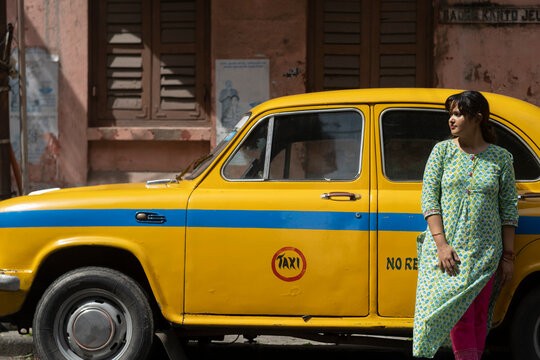 An Indian woman standing in front of a yellow taxi standing roadside