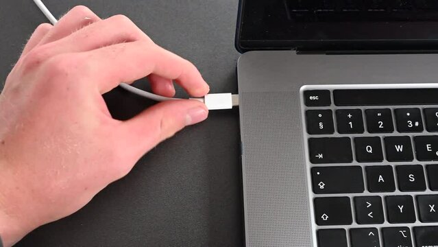 A laptop user plugs in a cable to charge his computer's battery