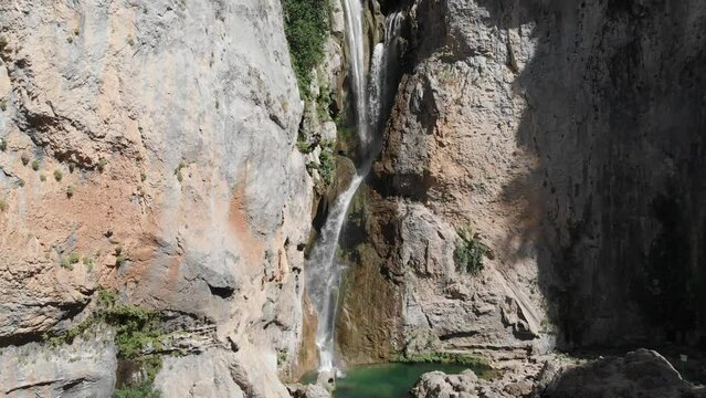Aerial dolly shot of an exotic waterfall in the mountains, as water curving into stone forming a pond.