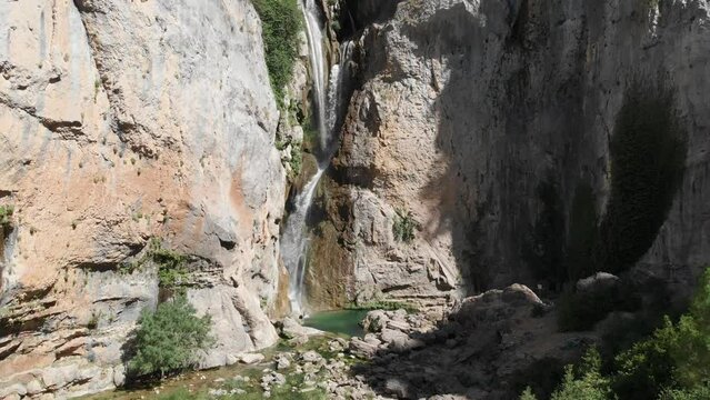 Ascending shot at remorse waterfall in the mountains, as water falls from heights, carving a pond in stone as forming the environment.
