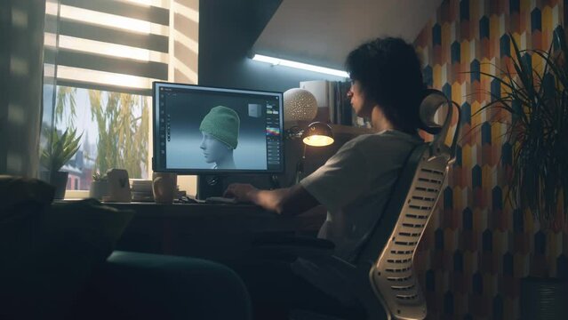 Guy sitting at the table and designing clothes in 3D modeling professional program on personal computer while working remotely from home