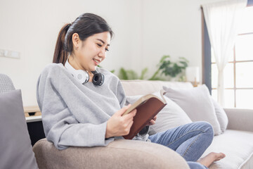 Obraz premium Beautiful Asian woman reading a book in her living room at home.