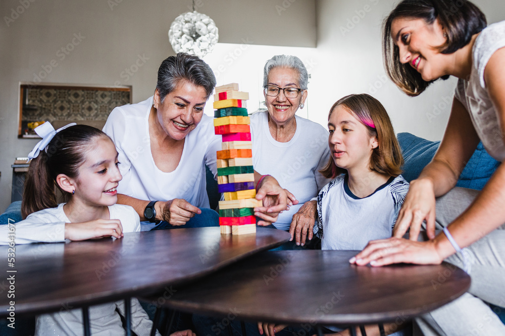 Poster Hispanic family playing Jenga game with grandmother and daughter at home, three generations of women in Mexico Latin America