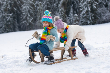 Children sledding, riding a sledge. Children son and daughter play in snow in winter. Outdoor kids...
