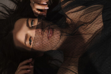 Sensual brunette woman playing with veil and looking at camera