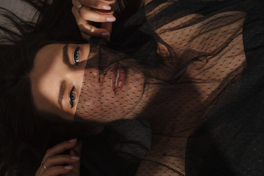 Sensual brunette woman playing with veil and looking at camera