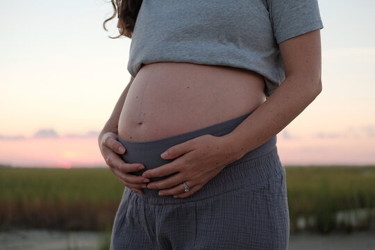 Pregnant woman outdoors holds her exposed belly.