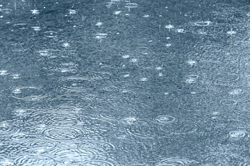 city pavement with raindrops and ripples in puddles during downpour