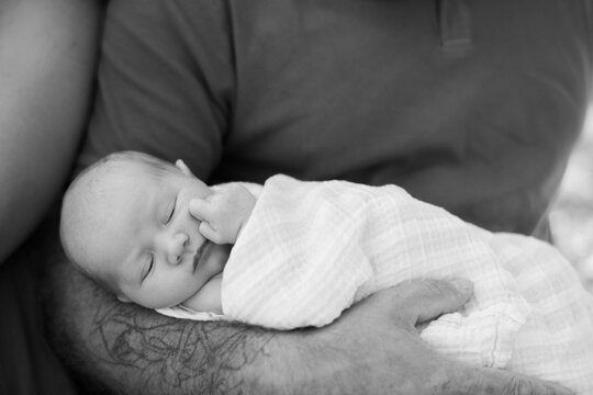close up of a swaddled baby in fathers arms 