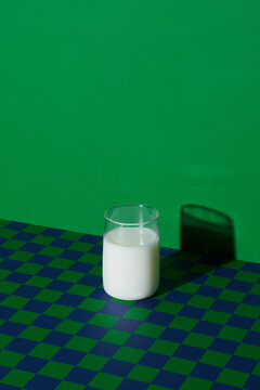 Cup of vegan milk on checkered table against green background