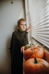 A boy looks out the window through the blinds waiting for friends to celebrate halloween
