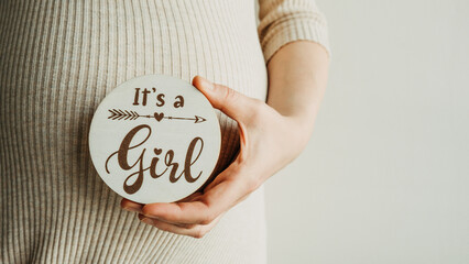Woman hands touching pregnant belly and holding wooden logo with text Its a girl. Banner, copy...